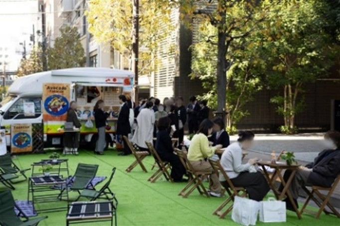 写真:芝生に設置されたキッチンカーと食事する人々